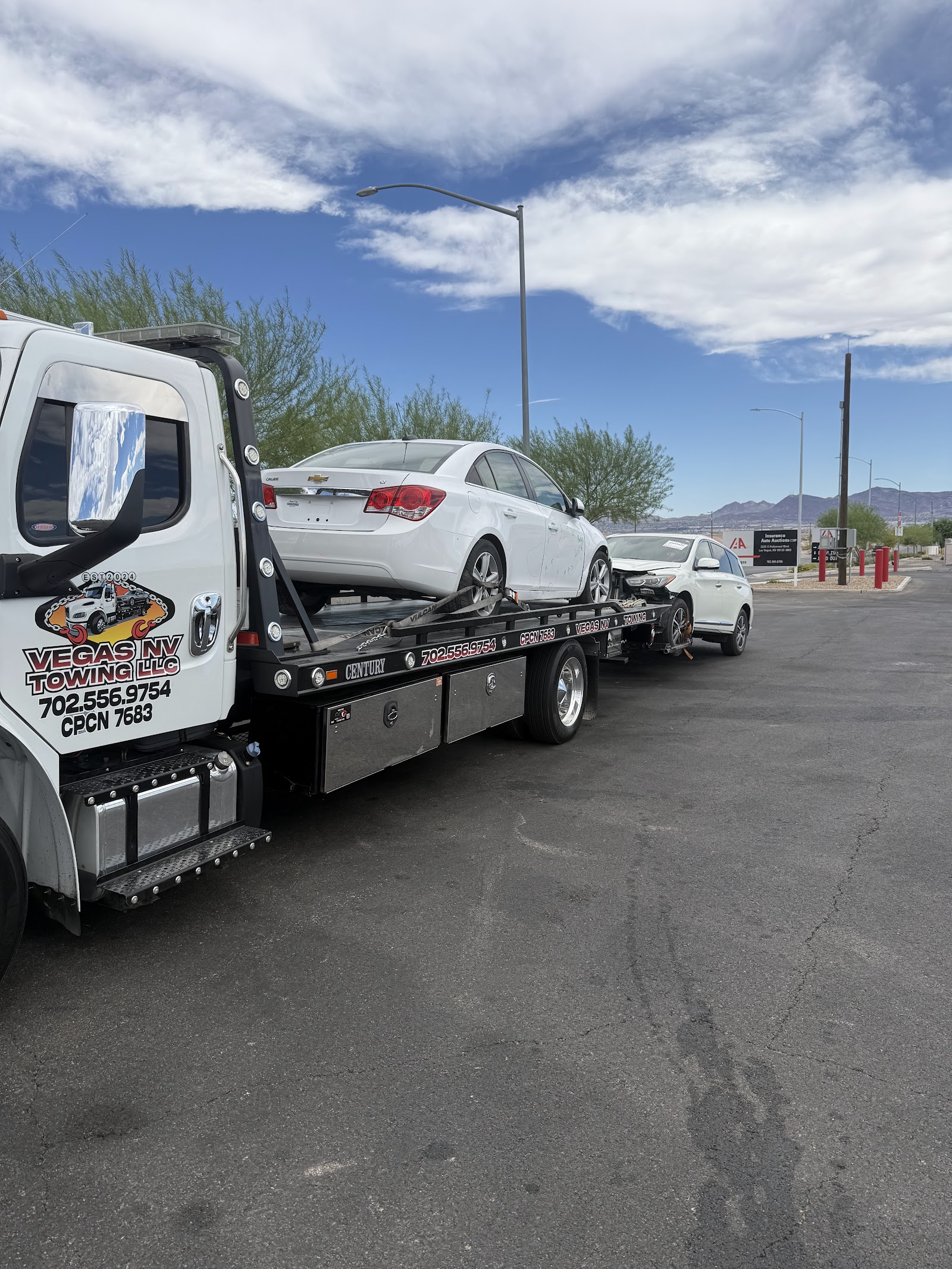 Vegas NV Towing flatbed truck hauling a white Chevrolet Cruze at an auto auction lot